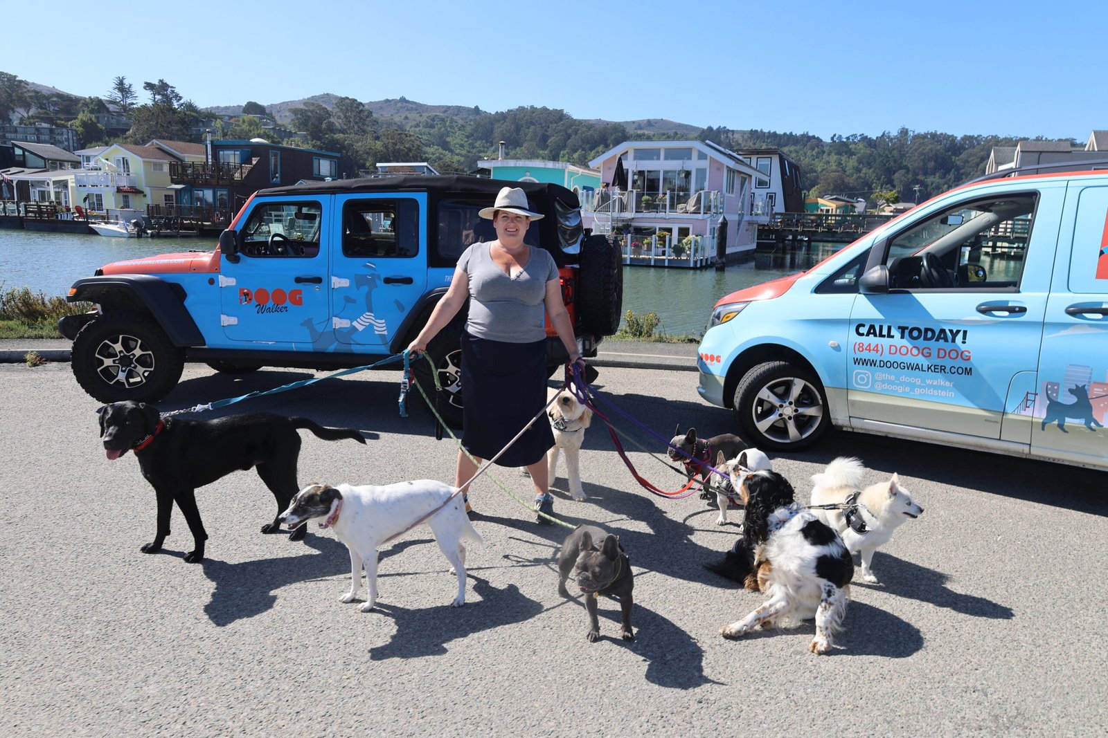 Professional dog walker with a group of dogs standing in front of The Doog Walker vehicles near the Sausalito houseboats in Marin County.