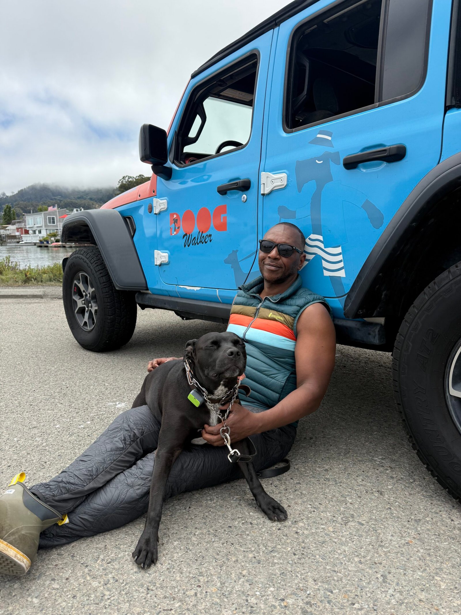 The Doog Walker team member relaxing with a black dog beside The Doog Walker vehicle during a Marin County group dog walk.